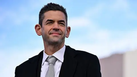 Getty Images A close up of Nasa Administrator Jared Isaacman, dressed in a black suit and striped silver tie, as he looks on during a rocket launch event 