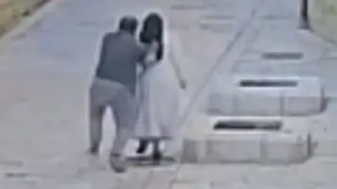 Grainy image from CCTV of a man from behind reaching out to push a nun as both walk in a street in Jerusalem (28/04/26)