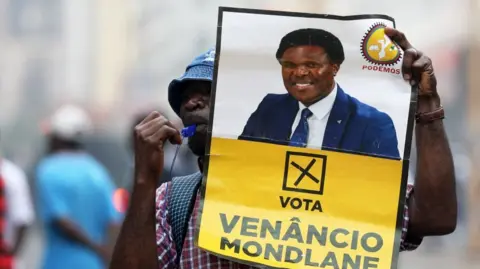 A man blowing a whistle holds a poster encouraging people to vote for Venancio Mondlane