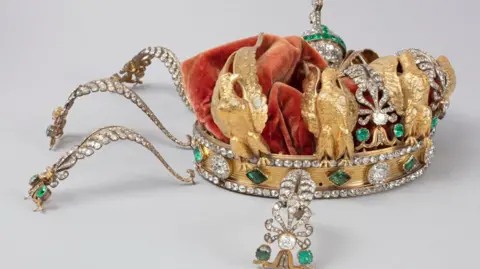 Louvre Museum The crown of French Empress Eugenie - a gold crown featuring diamonds, emeralds and golden eagles and a red velvet covering. Its decorations can be seen crushed inwards 
