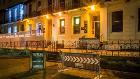 Under The Prom A lit up white terraced building at night time, with two black signs outside saying 'Under The Prom'. 