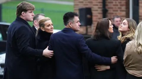 PA Media Terry Yorath's funeral with Gabby Logan looking over her shoulder with her family around her including son Reuben standing behind her with his arm around her 