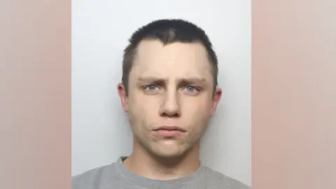 West Yorkshire Police George Wild is wearing a grey sweatshirt and is looking directly at the camera. He has short dark hair and is clean shaven