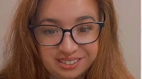 Ruthie O'Brien A woman with long red-brown hair is wearing glasses and smiling.
