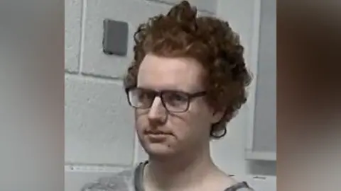 Thames Valley Police In a custody image, Bubb is shown in a grey T-shirt, wearing dark rimmed glasses. His curly red hair is longer.