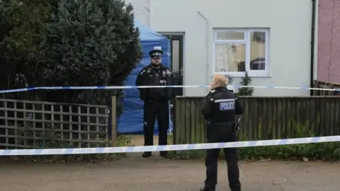 John Fairhall/BBC Police officers standing outside an home, blue tent erected in garden 