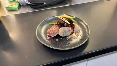 A meal on a dark plate featuring vegetables and garnishes arranged on a kitchen countertop.