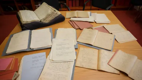 Trinity College Dublin A wooden table with books and papers on top. They are slightly off colour as they are aged.
