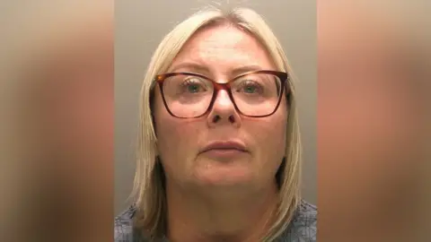 Police photograph of a bespectacled woman with fair hair. She is looking directly at the camera.