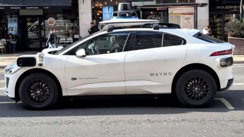 A Waymo car seen on a London road, driven by a driver