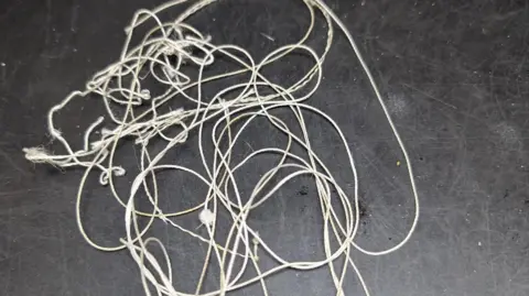 A white length of string tangled up on a table with a black surface.  