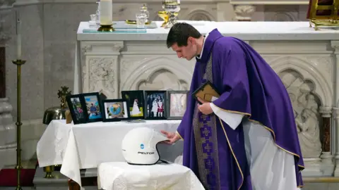 PA Media
Fr Sean Murphy places a rally helmet on the alter during the funeral mass for murdered Co Kerry farmer Michael Gaine