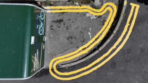 Eddie Mitchell An aerial shot of freshly painted double lines that loop back on themselves around a curb