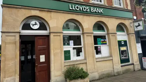 Elliot Deady/BBC Outside a branch of Lloyds Bank. It is brick building with a brown wooden door, arched windows and a green banner above with the words "LLOYDS BANK".