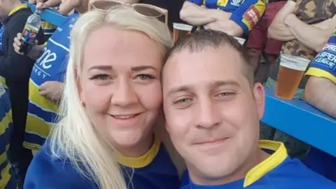 Handout Emma Miller and James Miller are smiling in this selfie taken at a Warrington Wolves game. They are both wearing the team jersey. Emma has long blonde hair and James has short brown hair. 
