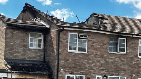 A house with a large blackened hole in its roof on a sunny day.