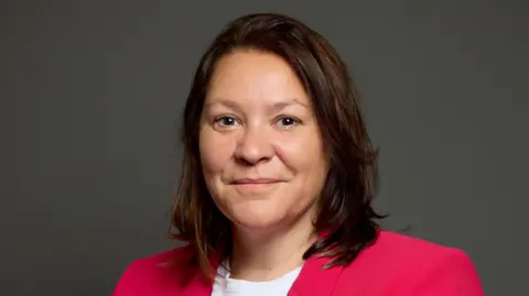 Anna Turley's official portrait. She has mid-length brown hair and is looking at the camera with a neutral expression. She is wearing a white shirt and pink blazer.