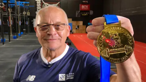 BBC Bernard Trybull in the gym, holding his gold medal up