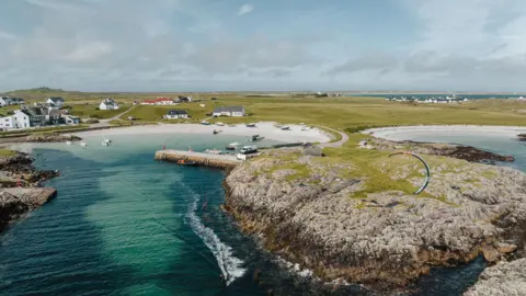 Getty Images White sandy beaches of Tiree. Clear blue waters. A smattering of white buildings and a large expanse of green fields. 