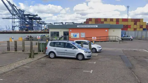 Cars parked in a car park in front of a small building. The building is orange and yellow.
