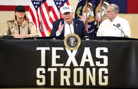 U.S. President Donald Trump, first lady Melania Trump and Texas Governor Greg Abbott participate in a roundtable with flags behind them and the motto Texas Strong on the table below them