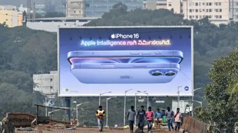 Getty Images pekerja berjalan di depan papan iklan iPhone 16 Apple di sepanjang jalan layang di Bengaluru pada 6 Januari 2025