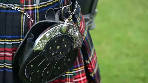Pacemaker A close up of a black leather pouch with silver trimmings that is attached to a kilt. Grass is behind the person. 
