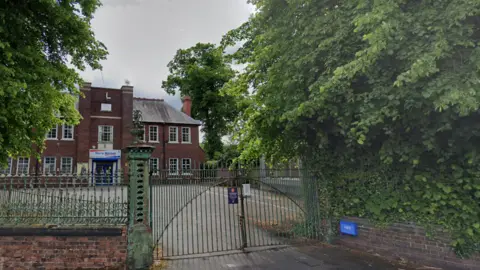 Google An exterior shot of Harry Mitchell leisure centre in Smethwick. Metal gates lead into a car park, on the other side of which is a large brick building with a sign above the entrance reading "Harry Mitchell".