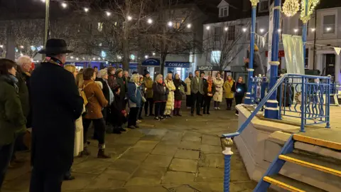 Erika Brichta A group of men and women stand at a vigil at Horsham bandstand 