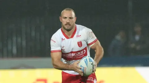 Karl Lawton carrying the ball in both hands but slightly towards his left-hand side playing for Hull KR
