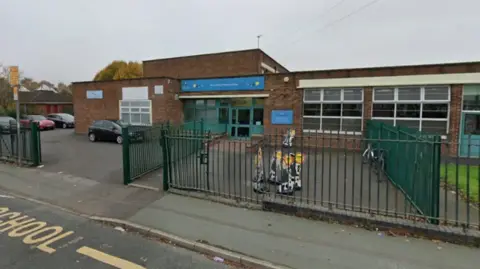 City of Wolverhampton The school as it is today is a one level building with a blue sign above the brick entrance with windows. There is a green gate at the roadside entrance.