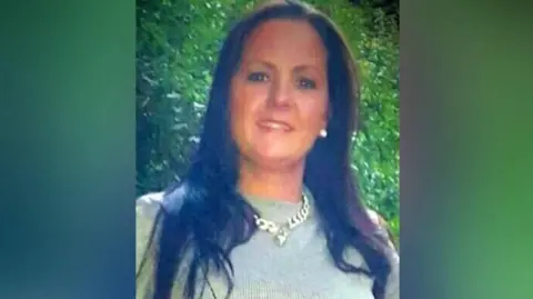 Family photo Victoria Thomas looking at the camera and smiling. She has straight black hair below her shoulder and it wearing a thick gold chain over a green shimmery top
