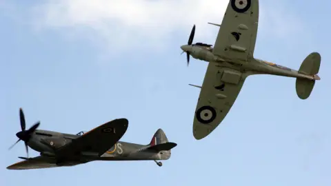 A group pair of Supermarine Spitfires fly in close order, above the Imperial War Museum airfield at Duxford. 