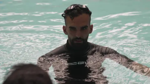 A man is standing in a swimming pool listening to an instructor