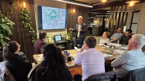 A7 Architects Men and women sat around a table looking at a screen with a blueprint plan 