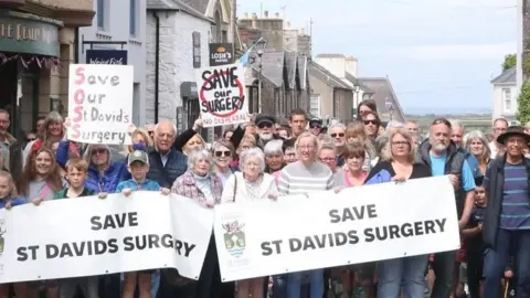 Campaigners in St Davids holding signs which say 'Save St Davids Surgery'