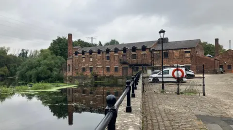 David Spereall/BBC An old industrial building situated on a canal. Large trees and shrubs can be seen next to the building.
