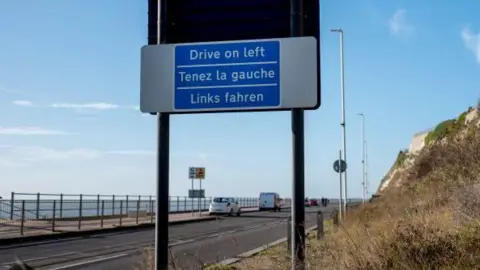 A blue sign reminding drivers to drive on the left side of the road.