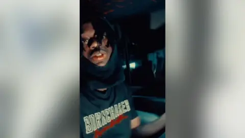 Instagram Boakye looks to camera with a hood over his head part of his lower face