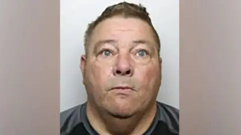 South Yorkshire Police Peter Lynch looking at the camera with a serious expression, wearing a black and grey top and in front of a grey background