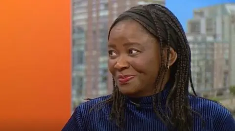 A woman in a blue jumper looks to her right at the interviewer on BBC .