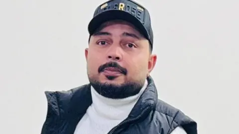 Rang & Rhythm Events handout Adeel Hashmi, who has a black beard and is wearing a white top, black gilet and black baseball cap. 