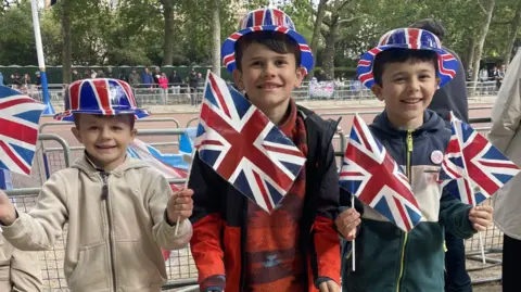 Three boys hold union flags along the mall celebrating VE day.