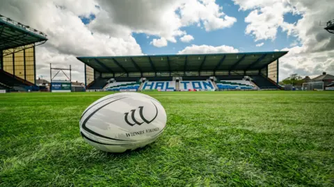 A rugby ball branded with the Widnes Vikings logo is positioned on the crash in the middle of the stadium. 