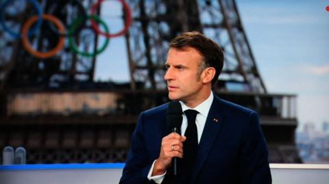 French President Emmanuel Macron hold a microphone while being interviewed in a TV studio