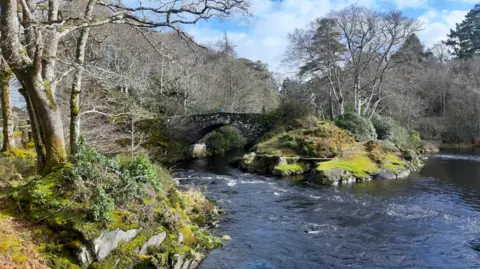 Jim and Sheila Beck A view of a bridge with water cascading underneath it, and the sun shining down
