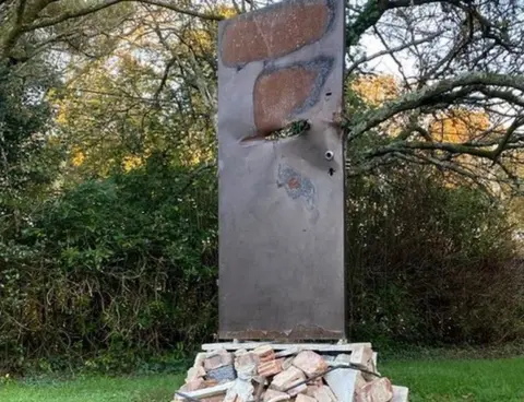 Robert Marshall Pile of rubble with silver-coloured door standing on top - it has a hole through it and large burn marks across the top.