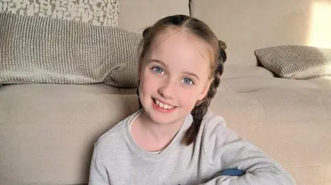 Selina Burns Eliza has brown hair inpigtail and a grey sweat shirt