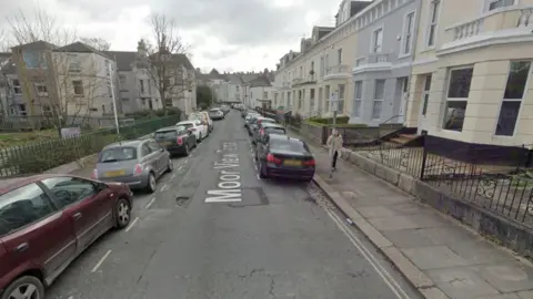 Google Google Maps image of Moor View Terrace. Cream and grey buildings are on the right-hand side of a narrow side street. A number of cars are parked on either side of the road.