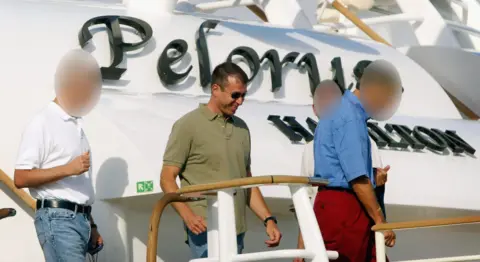 Roman Abramovich, sunglasses, jeans and a khaki polo shirt, with some colleagues, exiting the deck of Pelorus, the name of the boat is visible behind it.